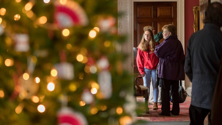 Images shows visitors through a doorway exploring the house at Stourhead, with a Christmas tree and lights visible in the foreground out of focus